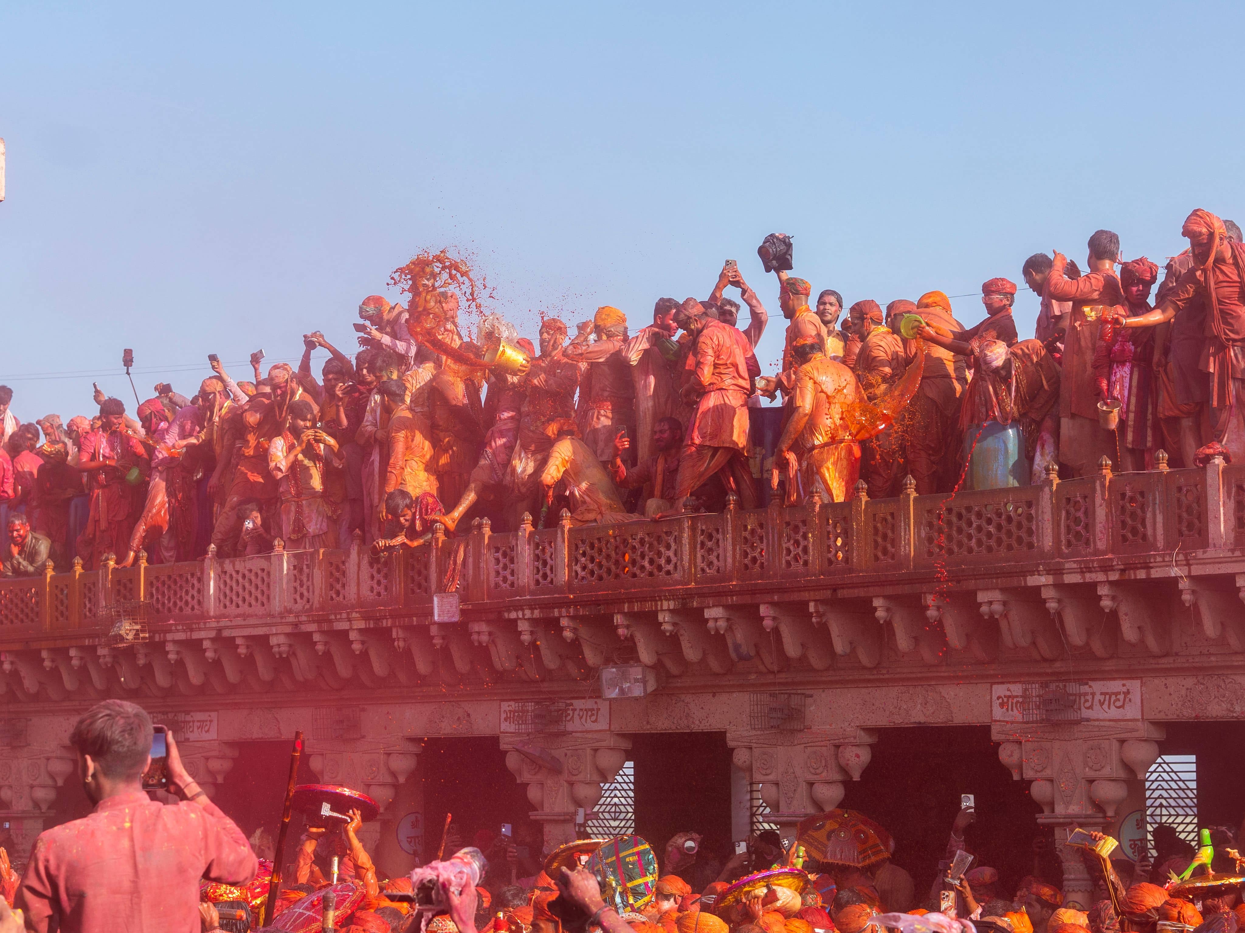 The crowded courtyard of Banke Bihari Temple in Vrindavan during Phoolon wali Holi with flower petals raining from the balcony