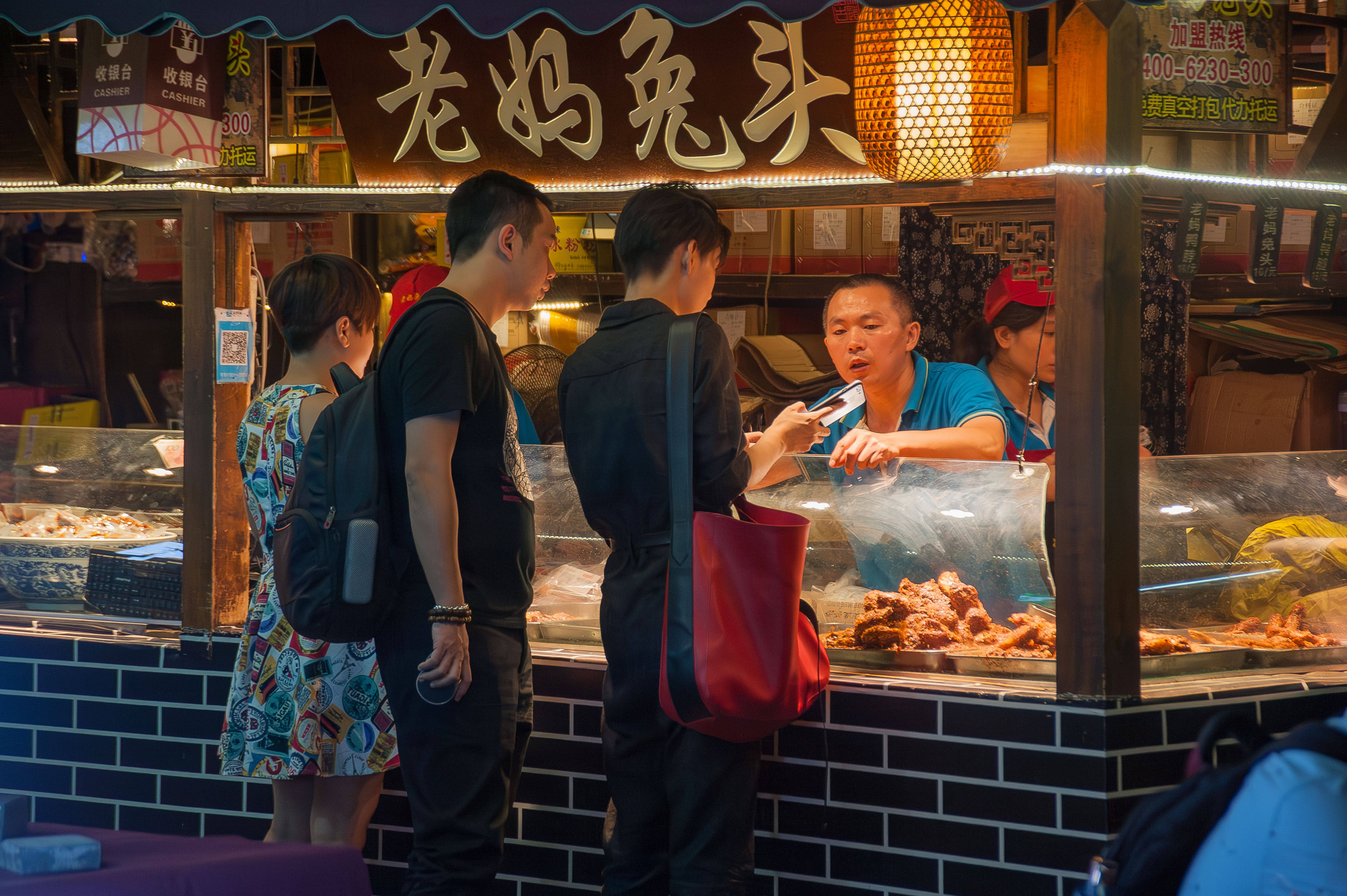 A visitor in a winter coat holding up a smartphone to scan a QR code at a lantern-lit entrance in Shanghai's Old City