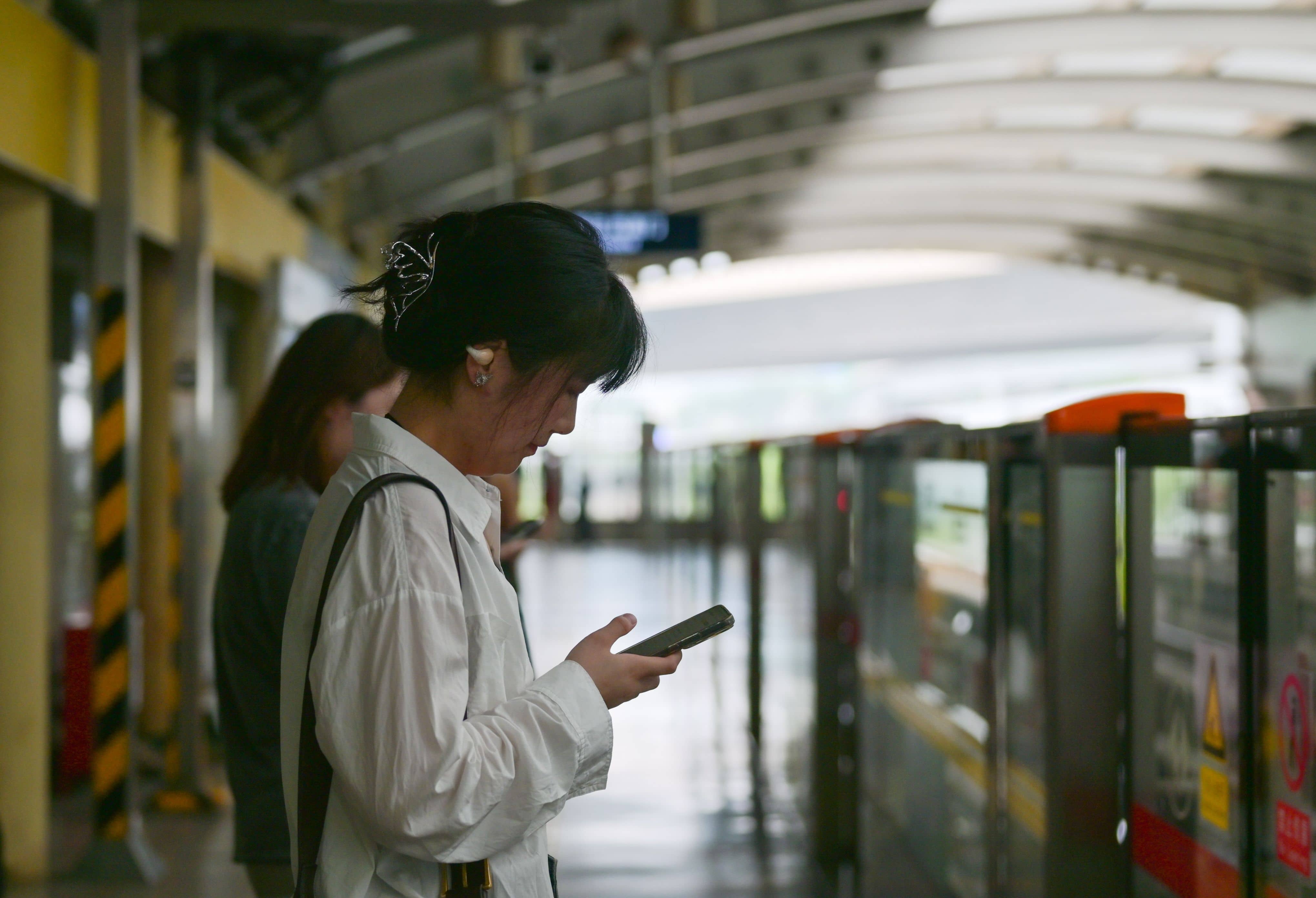 A visitor in rented Hanfu costume checking a smartphone on the Rainbow Bridge in Millennium City Park, Kaifeng, with crowds behind