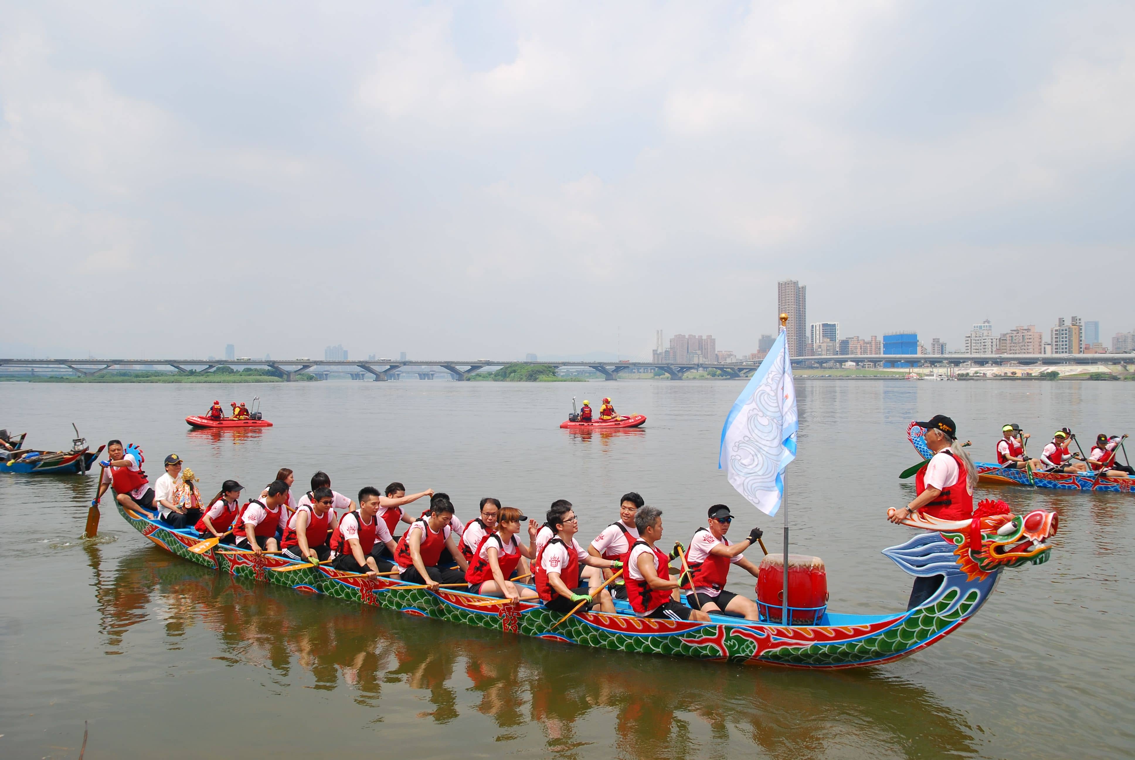 Spectators lining a concrete riverbank railing in Guangzhou watching dragon boats pass, with no ticket barriers in sight