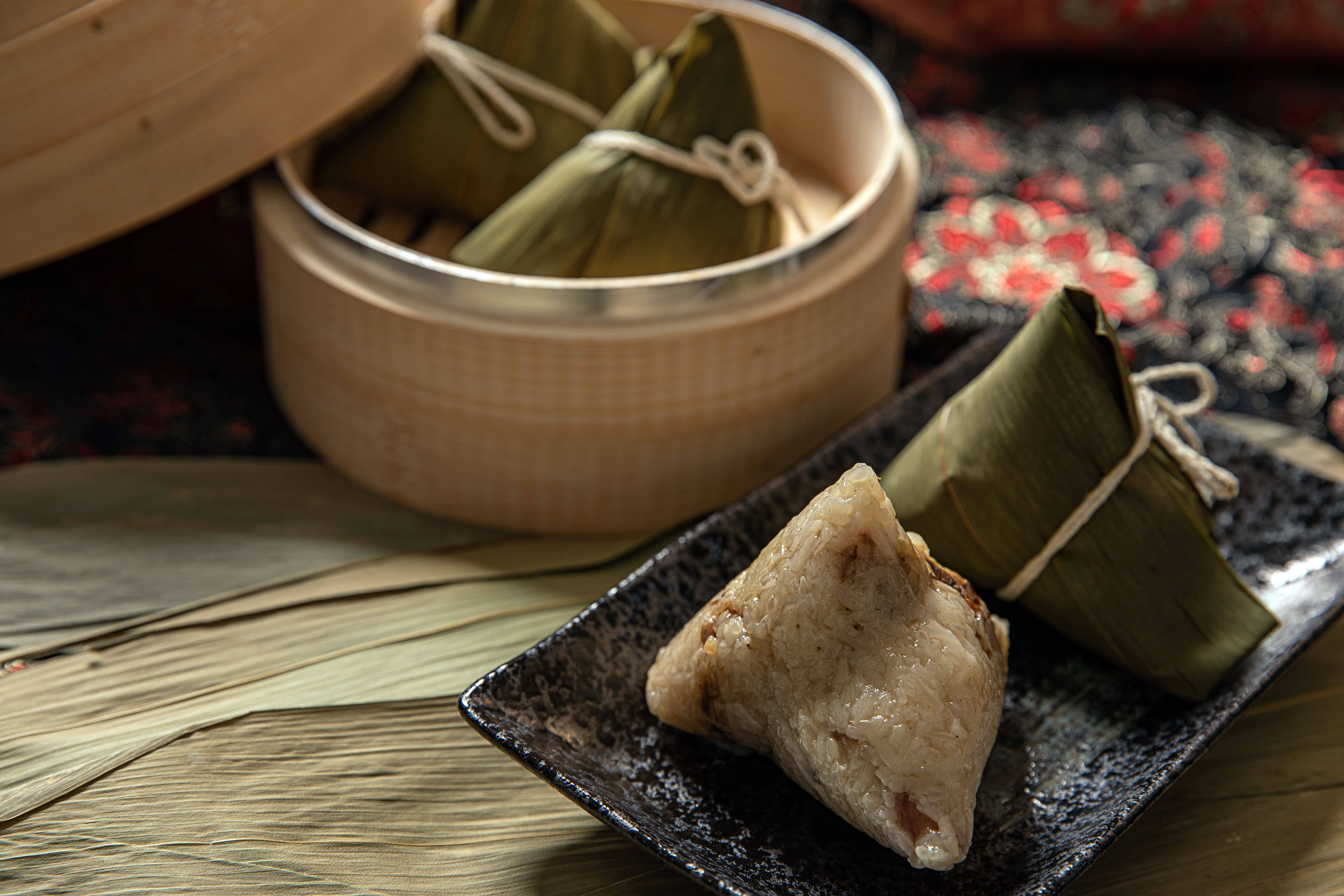 Close-up of freshly unwrapped zongzi, pyramid-shaped sticky rice dumplings in bamboo leaves, on a plate at a Cantonese table