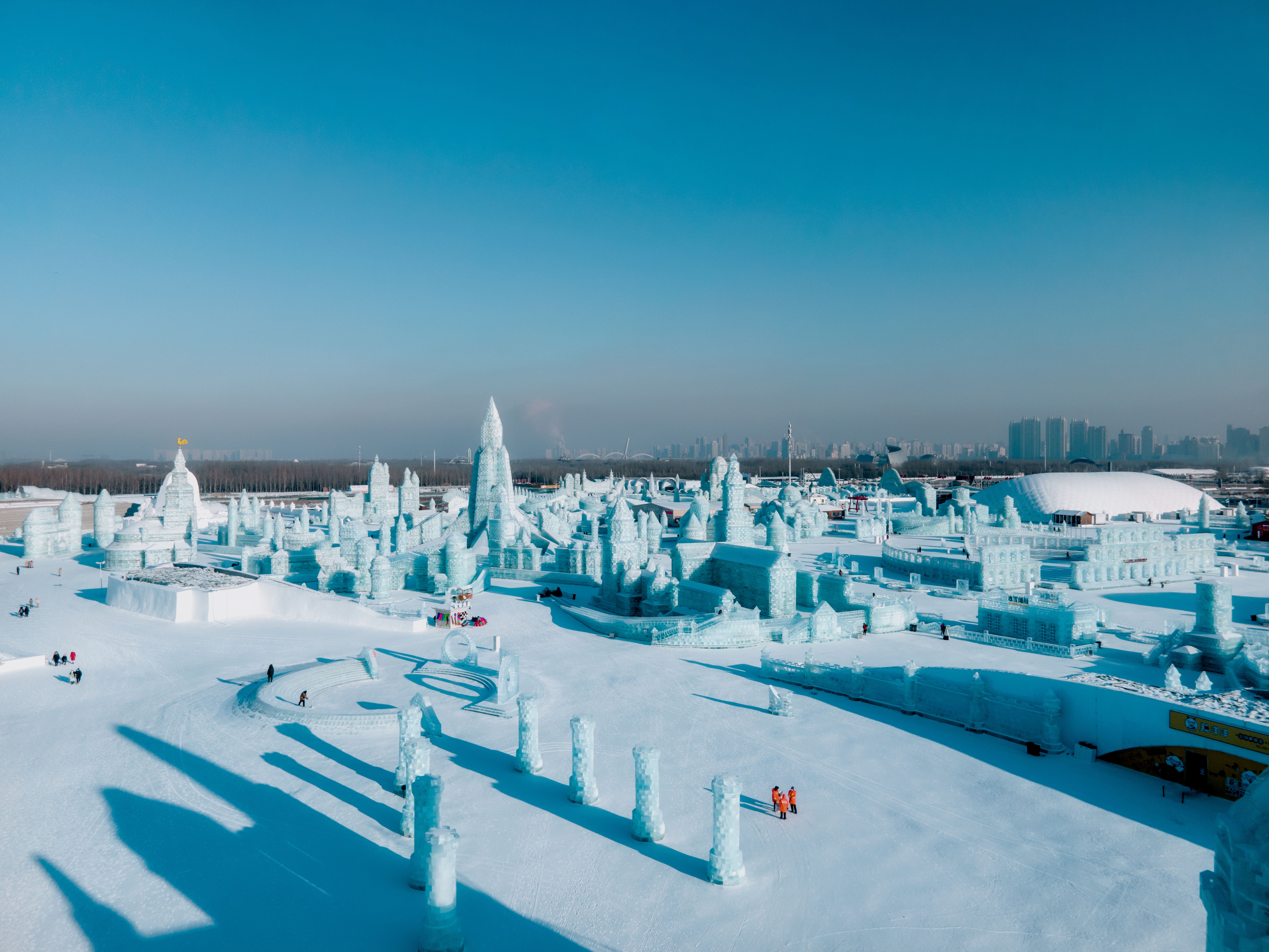 The main ice castle of Harbin Ice and Snow World lit in blue and purple at dusk with the crowd on the central plaza