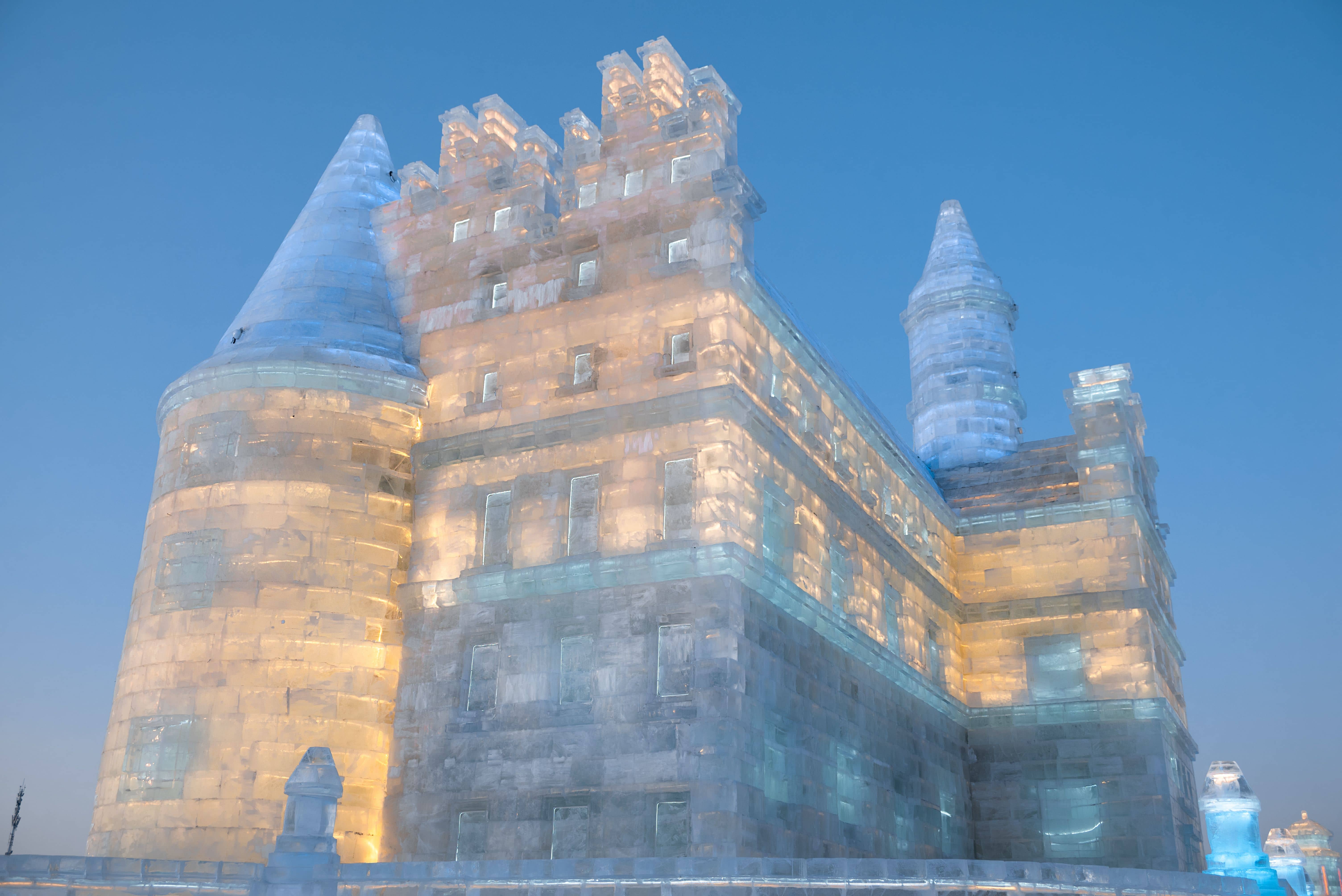 Visitors sliding down the long super ice slide at Harbin Ice and Snow World with lit ice towers glowing behind them