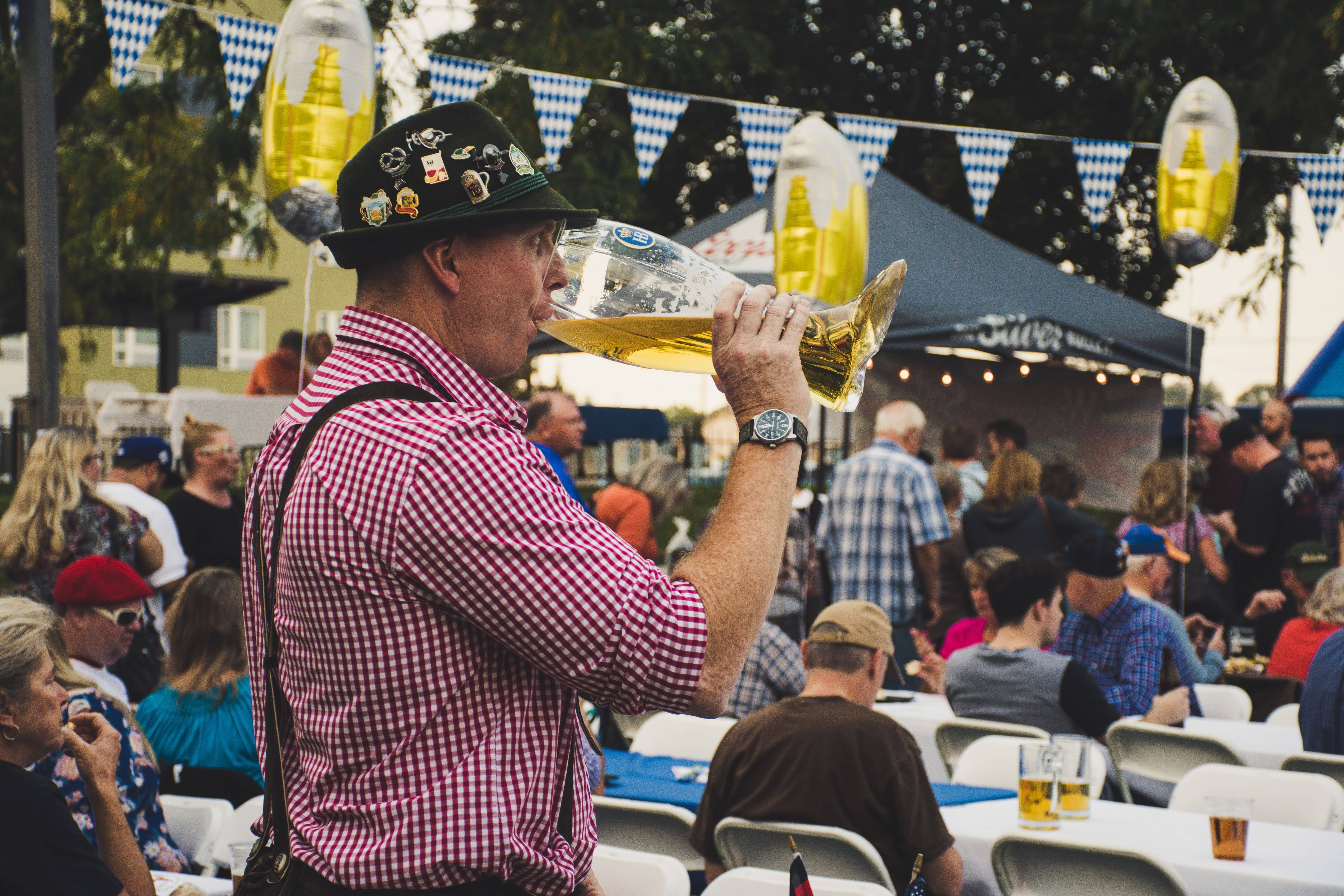 A server at Oktoberfest checking a reservation list at the entrance of a beer tent with a queue of visitors in dirndl and lederhosen