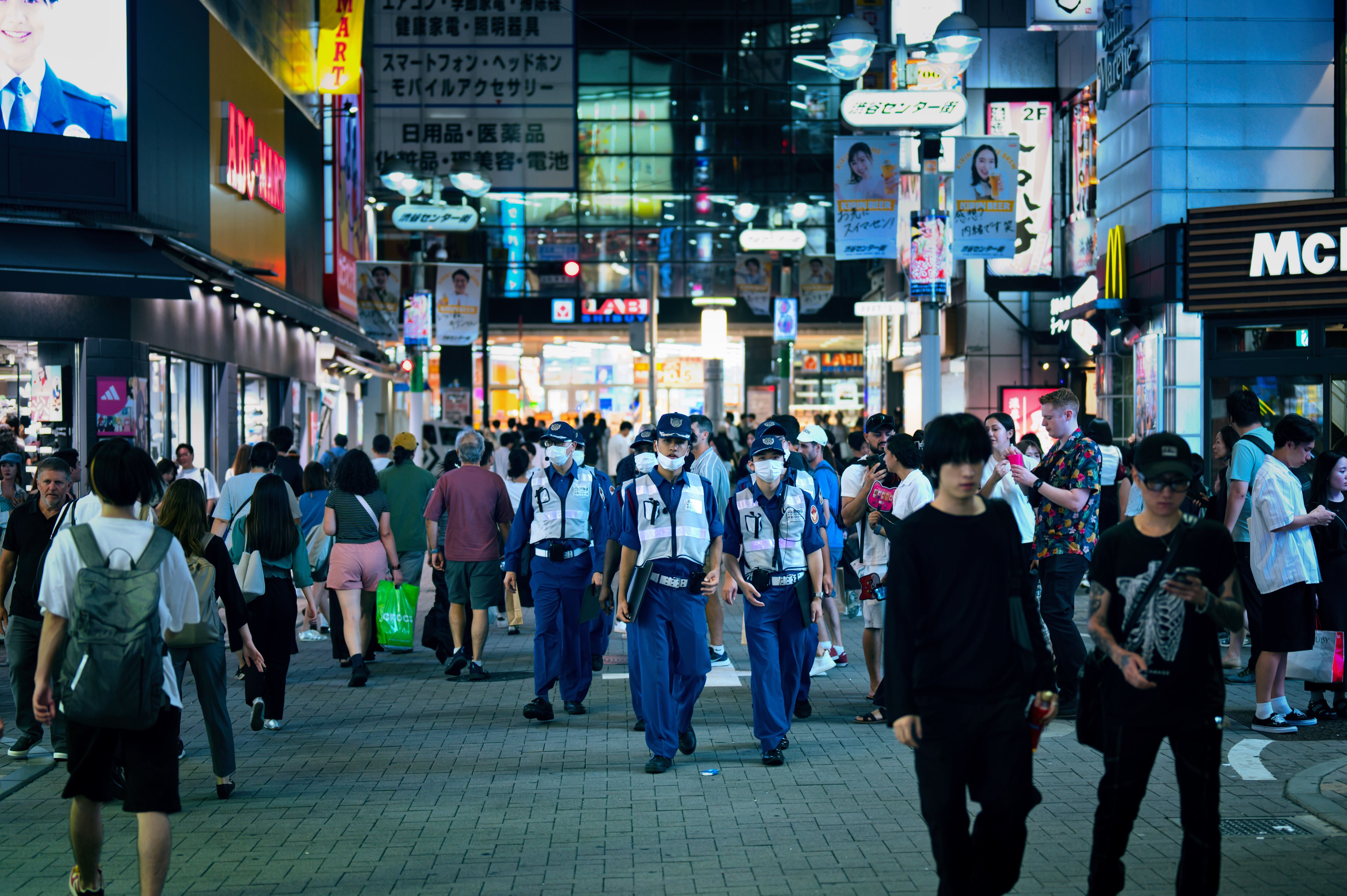Festival-goers in summer yukata with paper fans and bottled water walking along a sunlit Asakusa street on a hot July afternoon