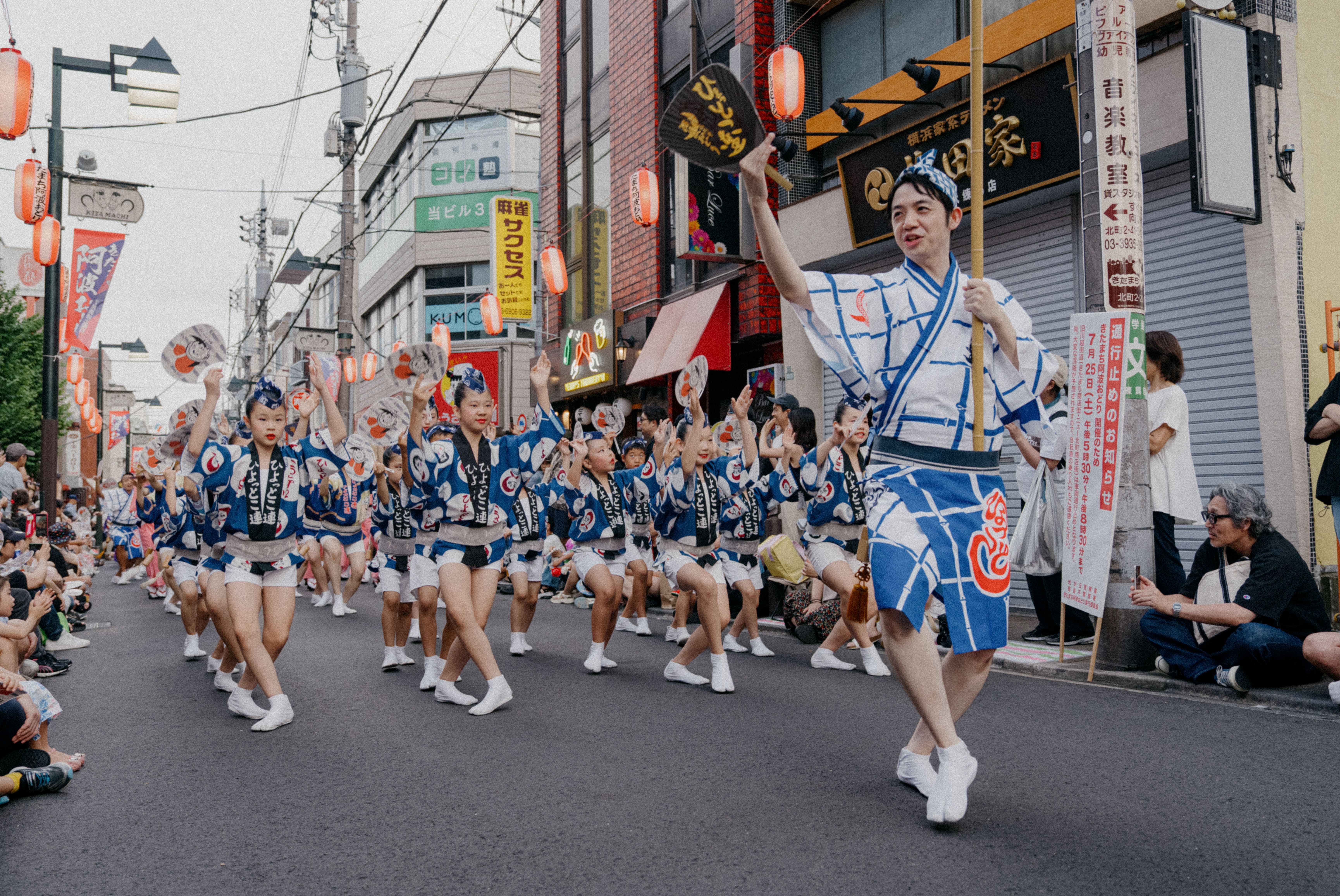 Spectators in yukata fanning themselves and holding cold drinks on a hot August evening at Awa Odori in Tokushima