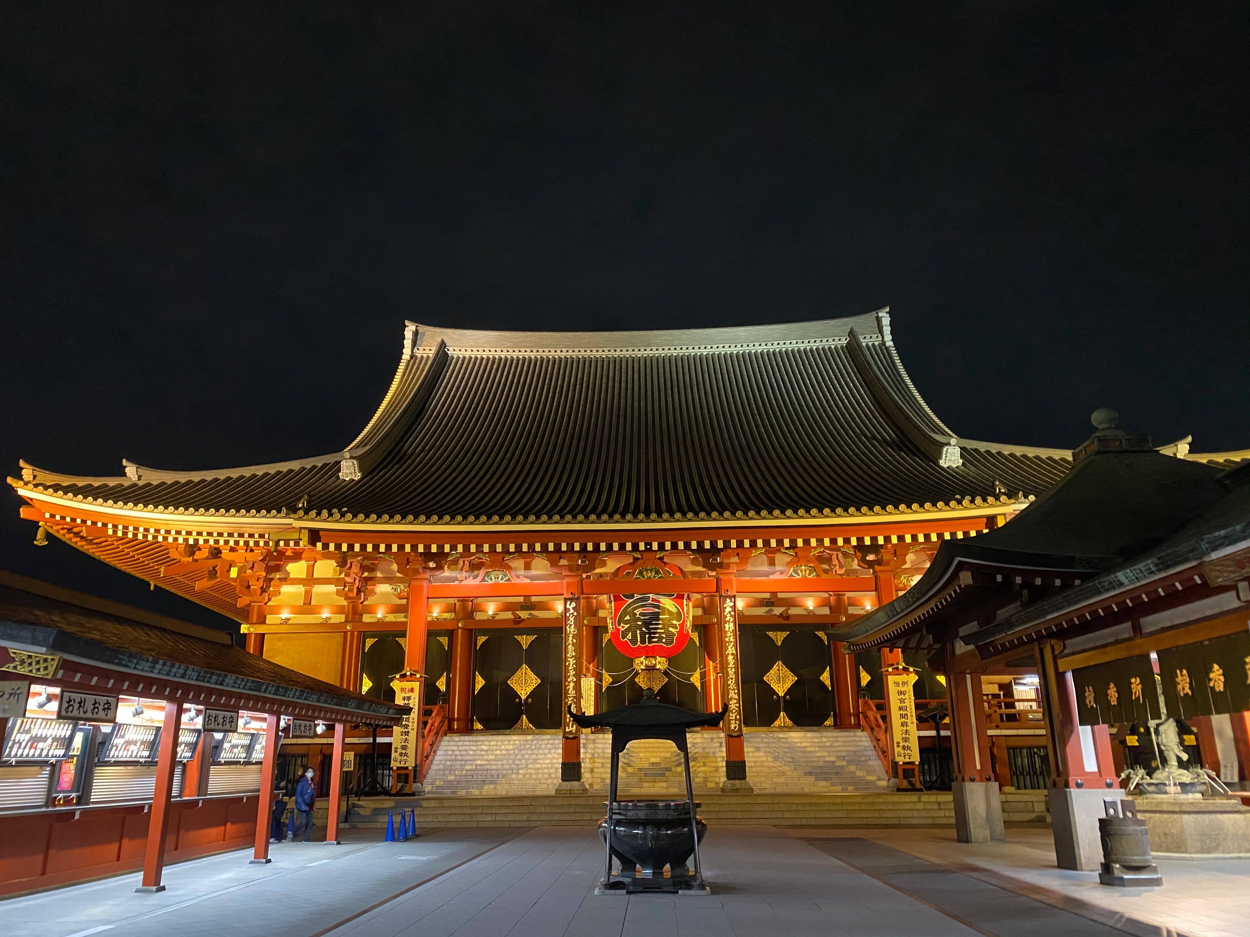 A quiet street of small hotels and ryokan in Asakusa at dusk with Senso-ji's five-storey pagoda visible behind the rooftops