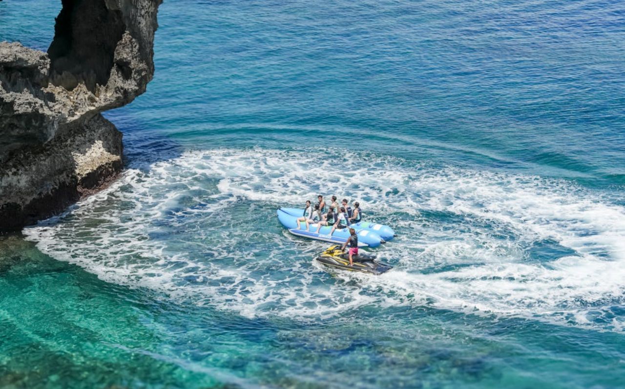 People riding inflatable banana boat near rocky Okinawa coastline