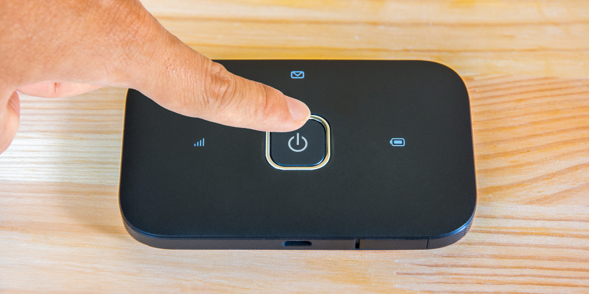 Close-up of a person pressing the power button on a pocket WiFi device