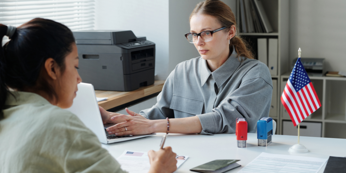 Người Việt đang phỏng vấn xin visa Mỹ thăm thân nhân tại Lãnh sự quán năm 2025, có cờ Mỹ và hồ sơ giấy tờ đầy đủ